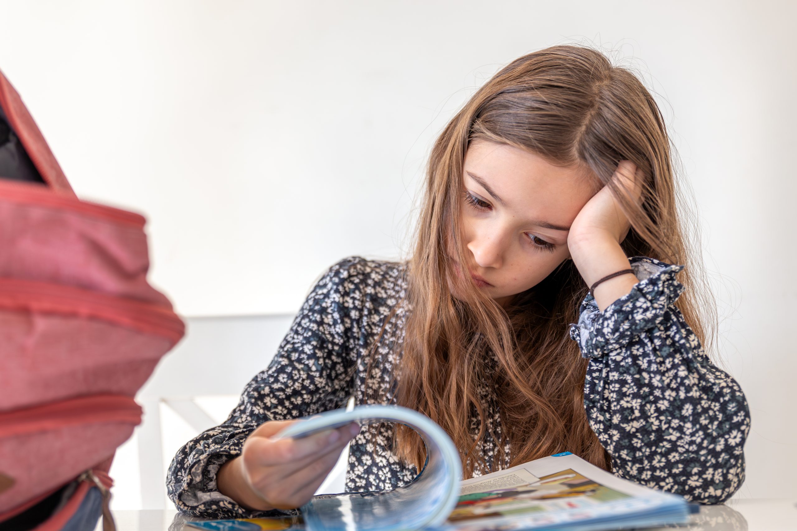 Nervis tornada escola Nena asseguda davant d’un llibre escolar, amb expressió preocupada i recolzant el cap sobre la mà, reflectint els nervis de la tornada a l’escola.